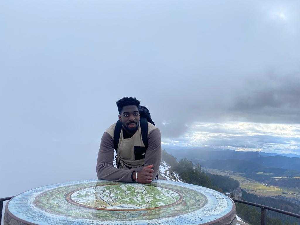 Photographie représentant le président et fondateur de l'entreprise Naymo face à un cercle représentant une carte d'une région avec comme arrière plan un paysage montagneux et des campagnes.
